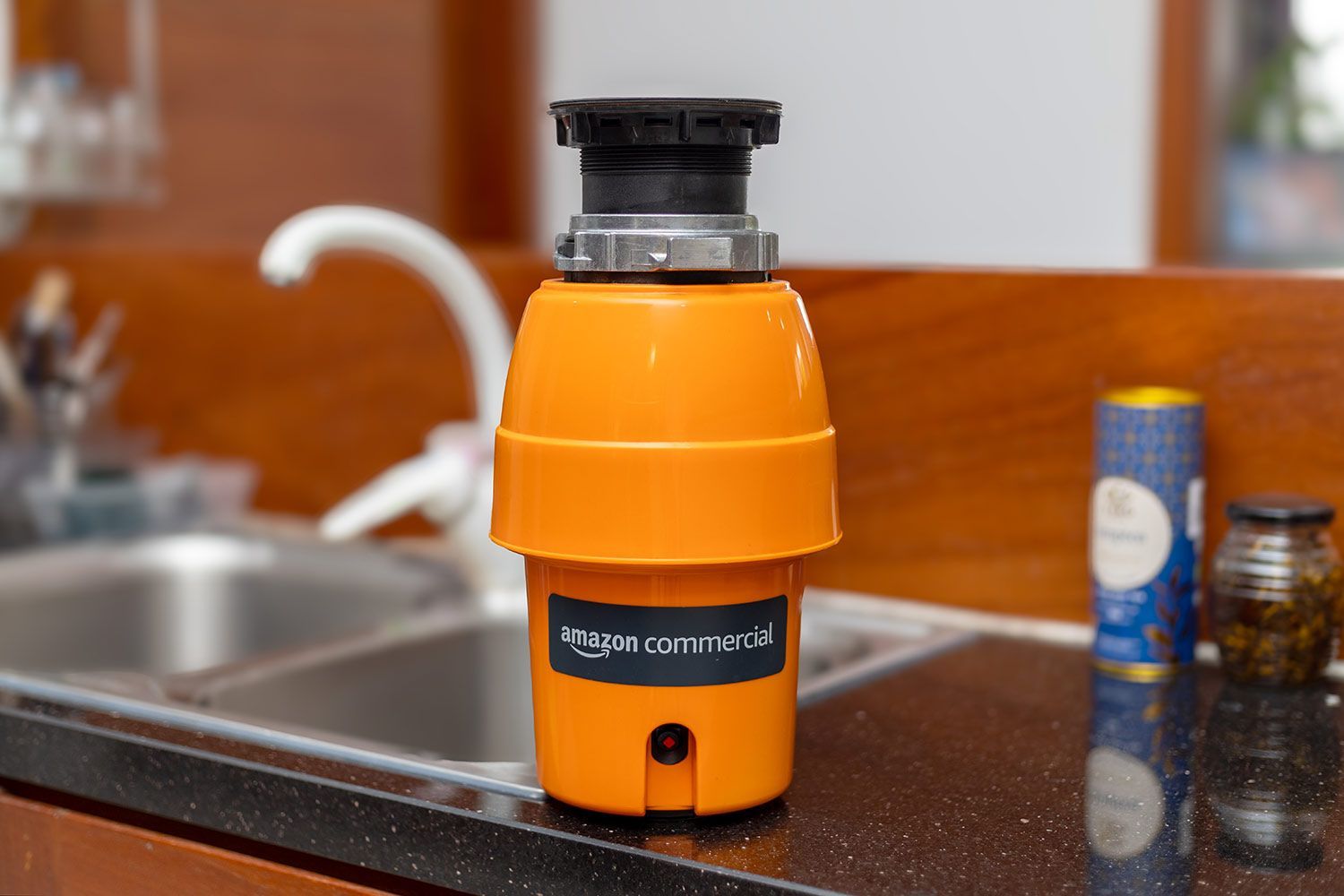 AmazonCommercial 1/2-Horsepower Garbage Disposal sitting on a kitchen countertop, next to a kitchen sink.