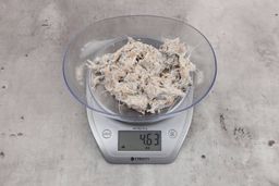 4.63 ounces of visible fish pin bones among mess of raw fibrous tissue on digital scale, on granite-looking table.