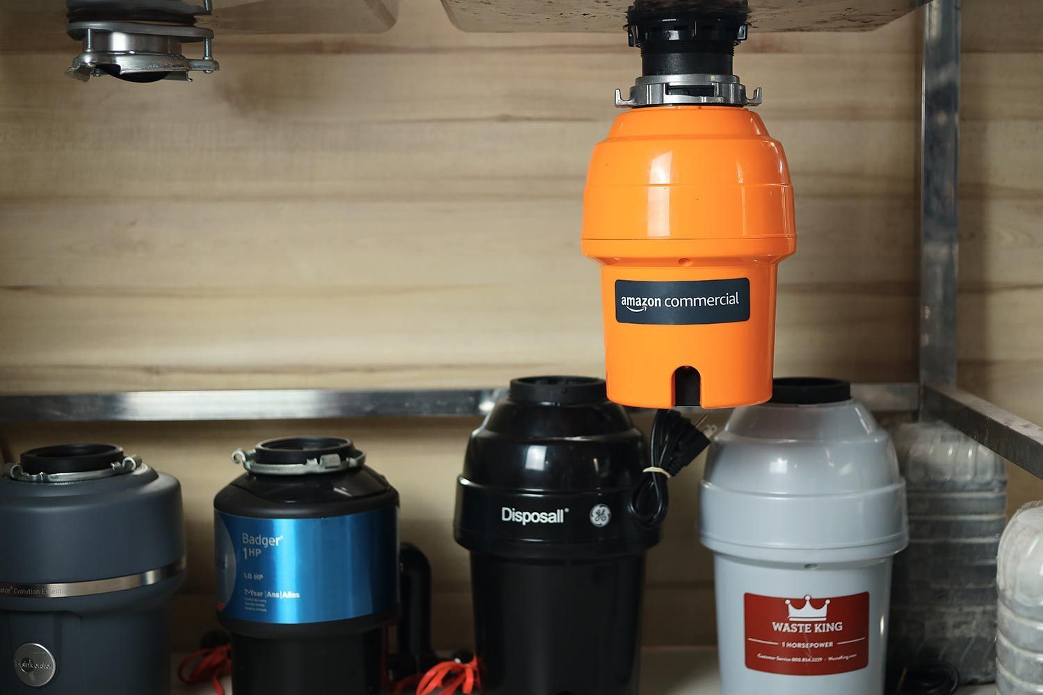 A garbage disposal from AmazonCommercial hangs from a steel sink. Several garbage disposals are in the background.