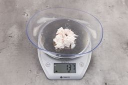 1.37 ounces of shredded fatty tissue and broken cartilage from chicken scraps on digital scale on granite-looking top.