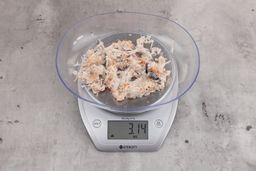  3.14 ounces of visible pin bones in a mass of raw meat and skin from fish scraps on digital scale on granite-looking top.