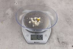 0.15 ounces of ground products from a garbage disposal, displayed on digital scale, placed on a granite-looking table. Shredded pieces of fish backbone and lemon peels.