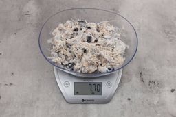 7.7 ounces of ground fish scraps from garbage disposal, displayed on digital scale, placed on granite-looking table. Visible pin bones among mess of raw fibrous tissue.