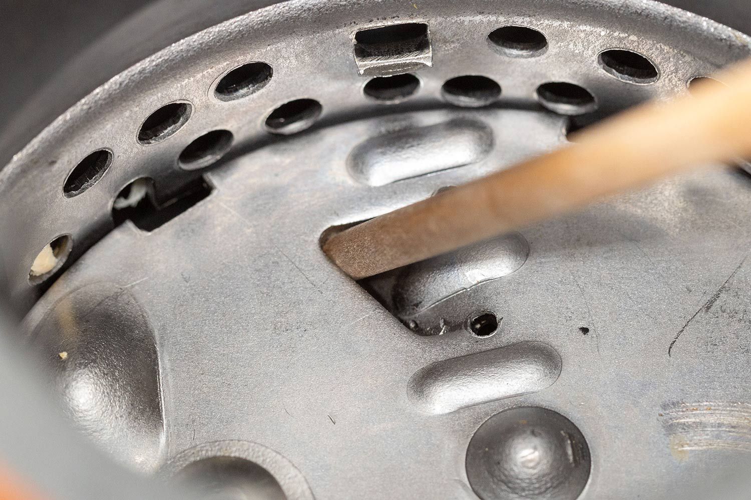 Inside view of permanent-magnet garbage disposal showing manual unjam mechanics with wooden stick in flywheel’s opening/gap.