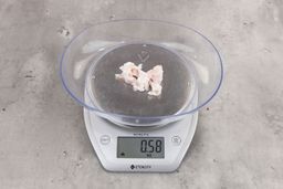 0.58 ounces of shredded fatty tissue and broken cartilage from chicken scraps on digital scale on granite-looking top.