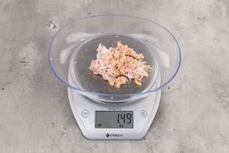 1.49 ounces of crushed chicken bone and cartilage, and shredded tendon and meat on digital scale on granite-looking top. 