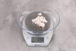 0.98 ounces of shredded fatty tissue and broken cartilage from chicken scraps on digital scale on granite-looking top.