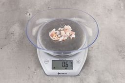 0.67 ounces of crushed chicken bone, shredded tendon, and fatty tissue on digital scale on granite-looking top.