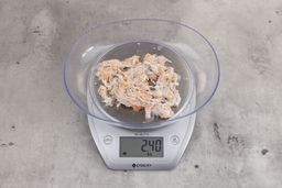 2.4 ounces of visible pin bones in a mass of raw meat and skin from fish scraps on digital scale on granite-looking top.