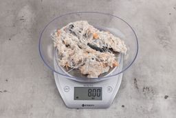 8 ounces of visible pin bones in a mass of raw meat and skin from fish scraps on digital scale on granite-looking top.