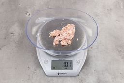 1.01 ounces of ground chicken scraps from garbage disposal, displayed on digital scale, placed on granite-looking table. Mess of shredded tendons and pieces of shredded bones.