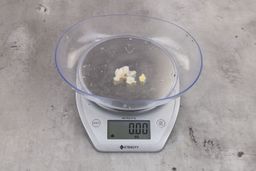 Almost 0 ounces of ground products from garbage disposal, displayed on digital scale, placed on granite-looking table. Pieces of shredded dietary fiber.