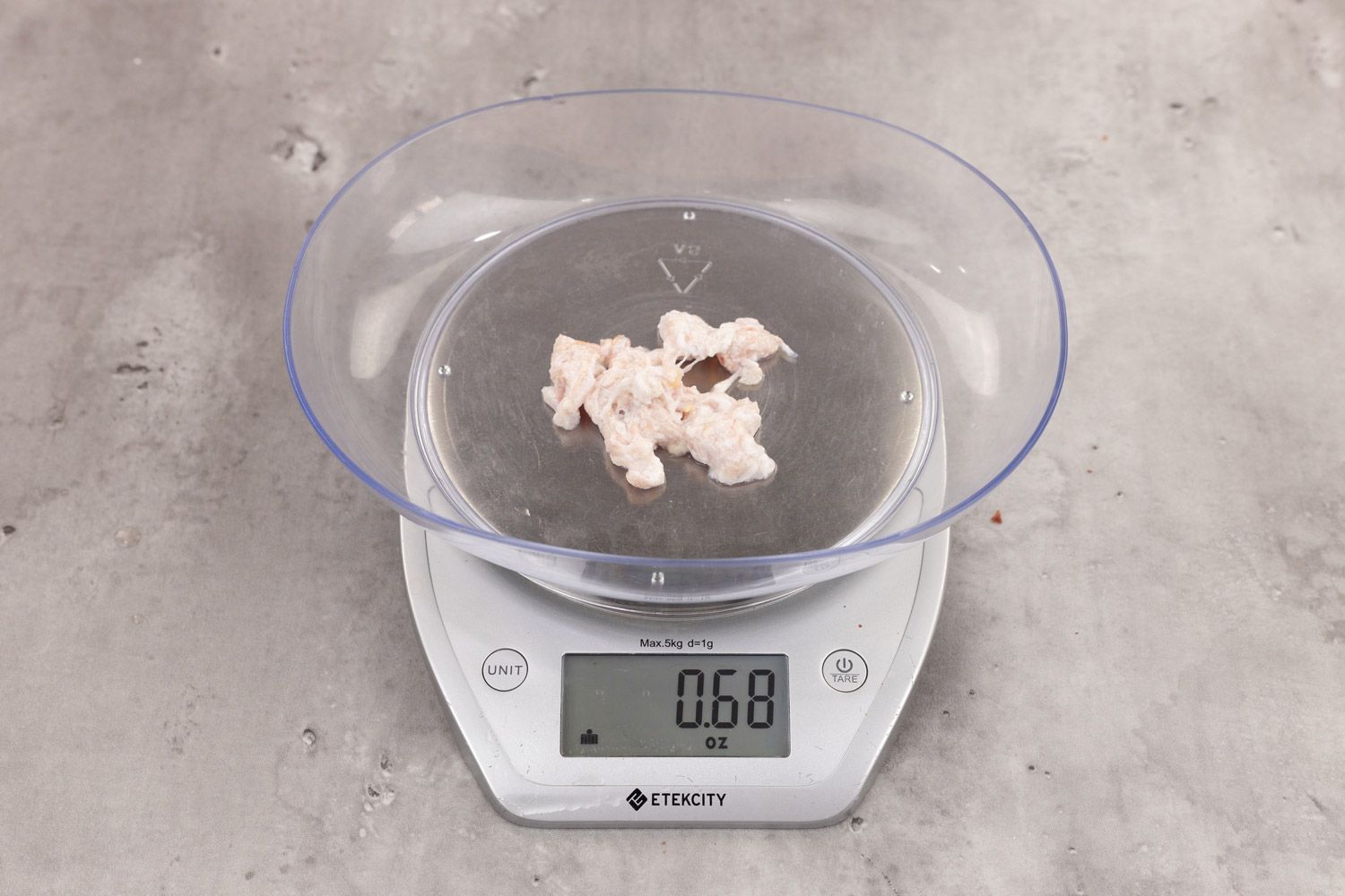 0.68 ounces of ground chicken scraps from garbage disposal, displayed on digital scale, placed on granite-looking table. Mess of shredded soft tissue and few pieces of shredded bones.