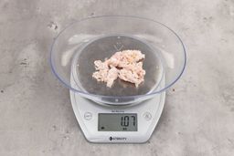 1.07 ounces of ground chicken scraps from a garbage disposal, displayed on a digital scale, placed on a granite-looking table. Mess of fibrous soft tissue and pieces of shredded bones.