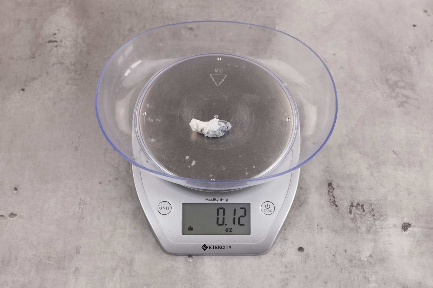 0.12 ounces of ground fish scraps from a garbage disposal, displayed on digital scale, placed on granite-looking table. Small mess of shredded fish backbone and skin.