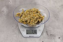 7.16 ounces of ground products from a garbage disposal, displayed on a digital scale, placed on a granite-looking table. Mess of assorted scraps, including fibers, bones, etc.