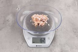 1.62 ounces of shredded soft tissue and pieces of shredded chicken bone, on digital scale, on granite-looking top.