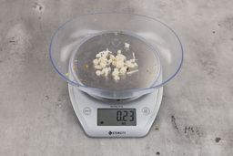 0.23 ounces of shredded pieces of fish backbone, dietary fibers, and fish meat, on digital scale, on granite-looking top.