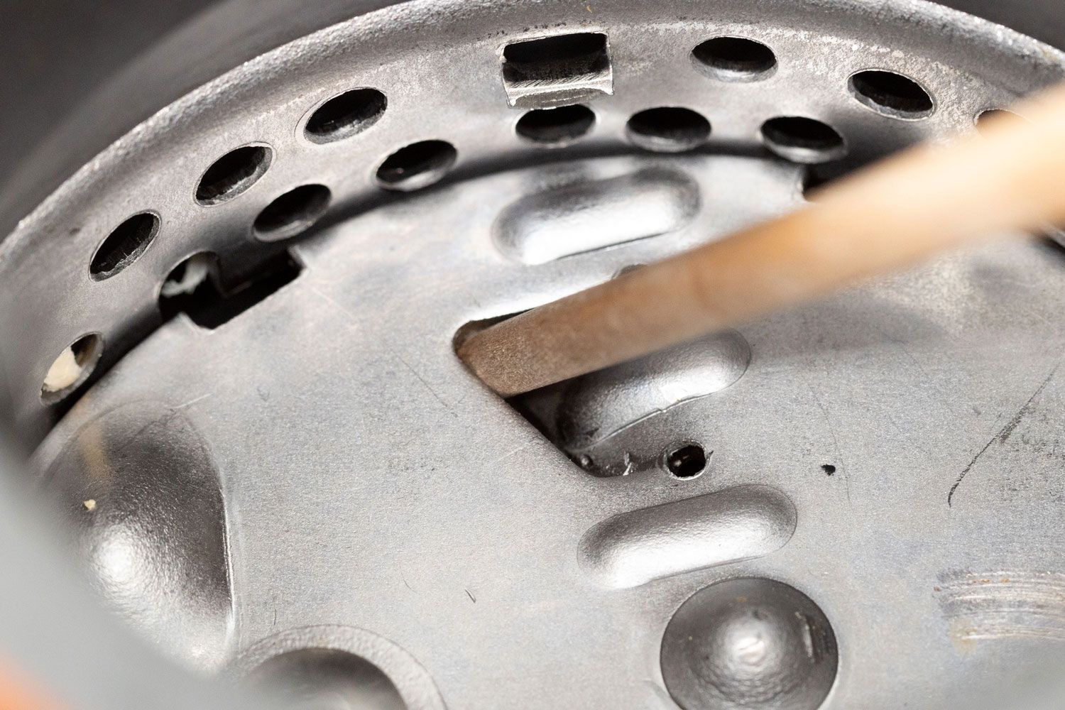 Inside view of permanent-magnet garbage disposal showing manual unjam method with wooden stick in flywheel’s opening/gap.