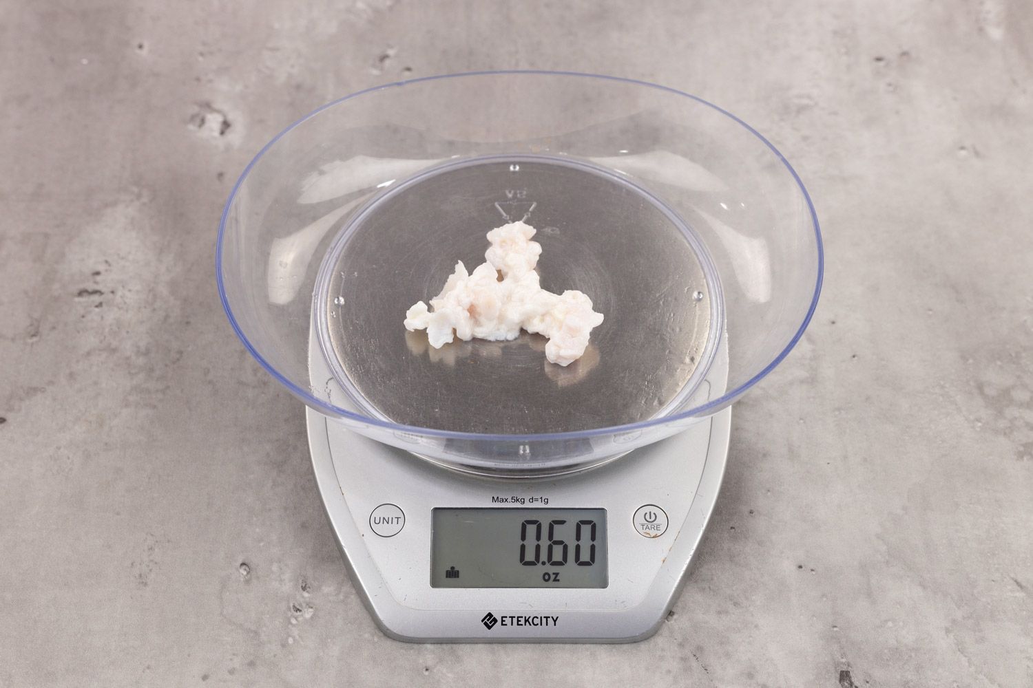 0.6 ounces of ground chicken scraps from garbage disposal, displayed on digital scale, placed on granite-looking table. Pieces of shredded cartilage among mess of soft tissue.