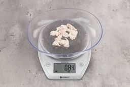 0.84 ounces of fibrous soft tissue and few pieces of shredded chicken bones, on digital scale, on granite-looking top.