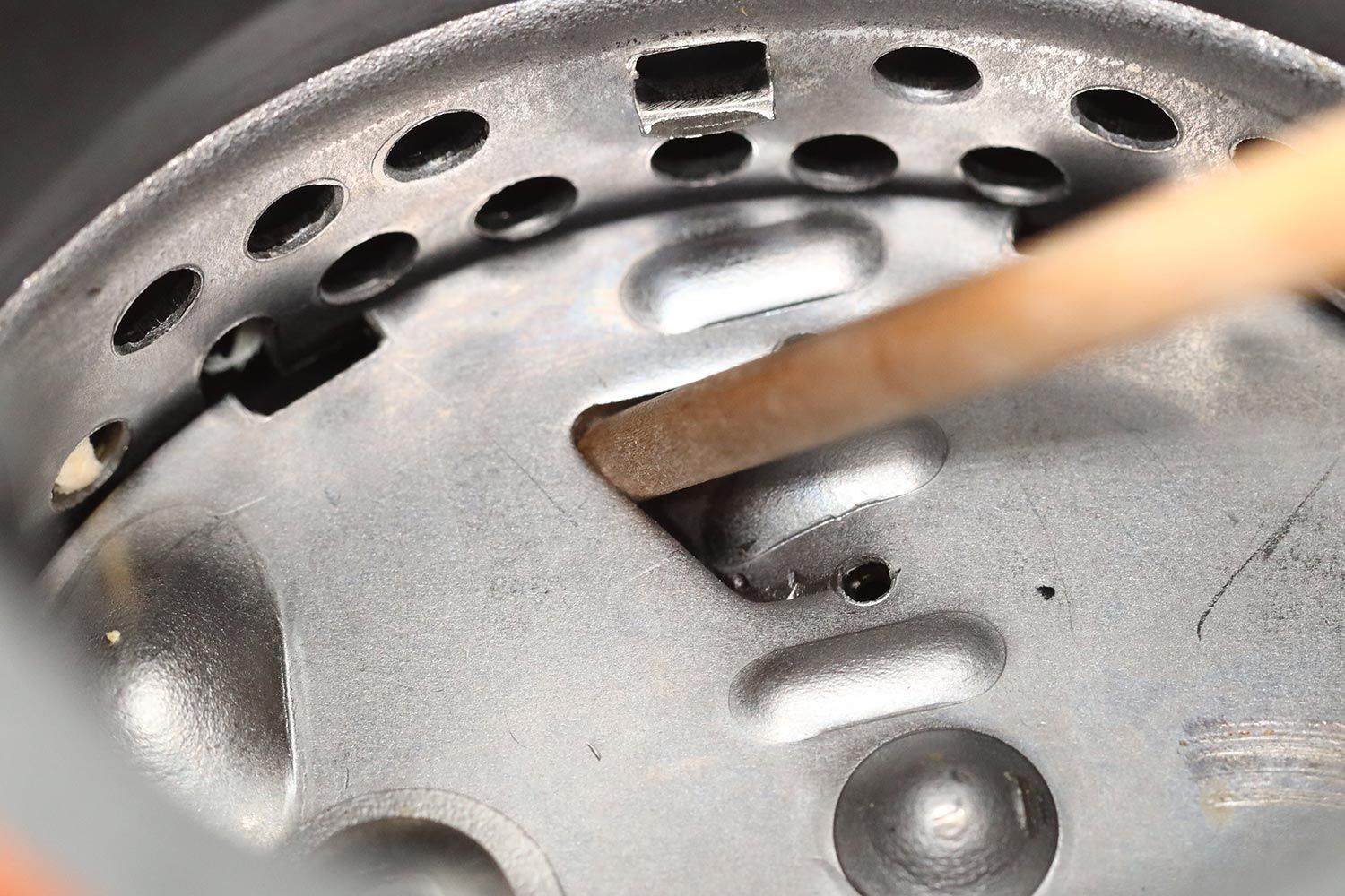 Inside view of permanent-magnet garbage disposal showing manual unjam method with wooden stick in flywheel’s opening/gap.