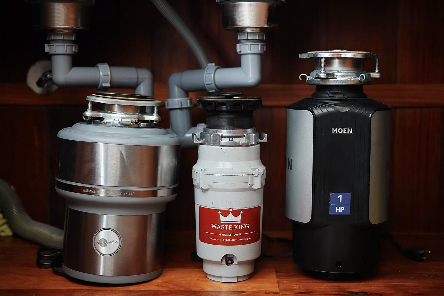 Garbage disposals stand next to one another, including an InSinkErator Evolution Excel, a Waste King L1001, and a Moen GX100C 