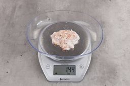 1.44 ounces of fibrous soft tissue and few pieces of shredded chicken bones, on digital scale, on granite-looking top.