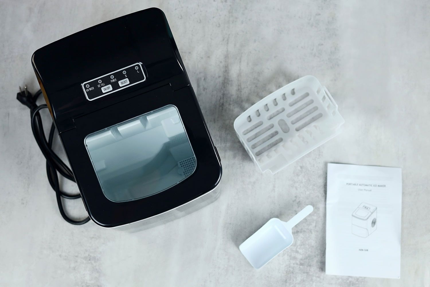 Top down view of the unboxed AGLucky Ice Maker HZB-12/B with an ice basker, ice scoop, and user manual pictured slightly off to the left.