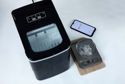 The AGLucky Ice Maker HZB-12/B on a countertop with a glass bowl containing nine ice bullets in front showing a net weight of 54 grams, and a stopwatch to the upper right showing 8 min 21 sec for the time to make one round of ice bullets.