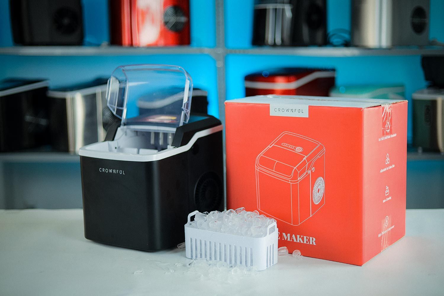 The Crownful ice maker on a countertop next to its box and a full basket of ice in front.