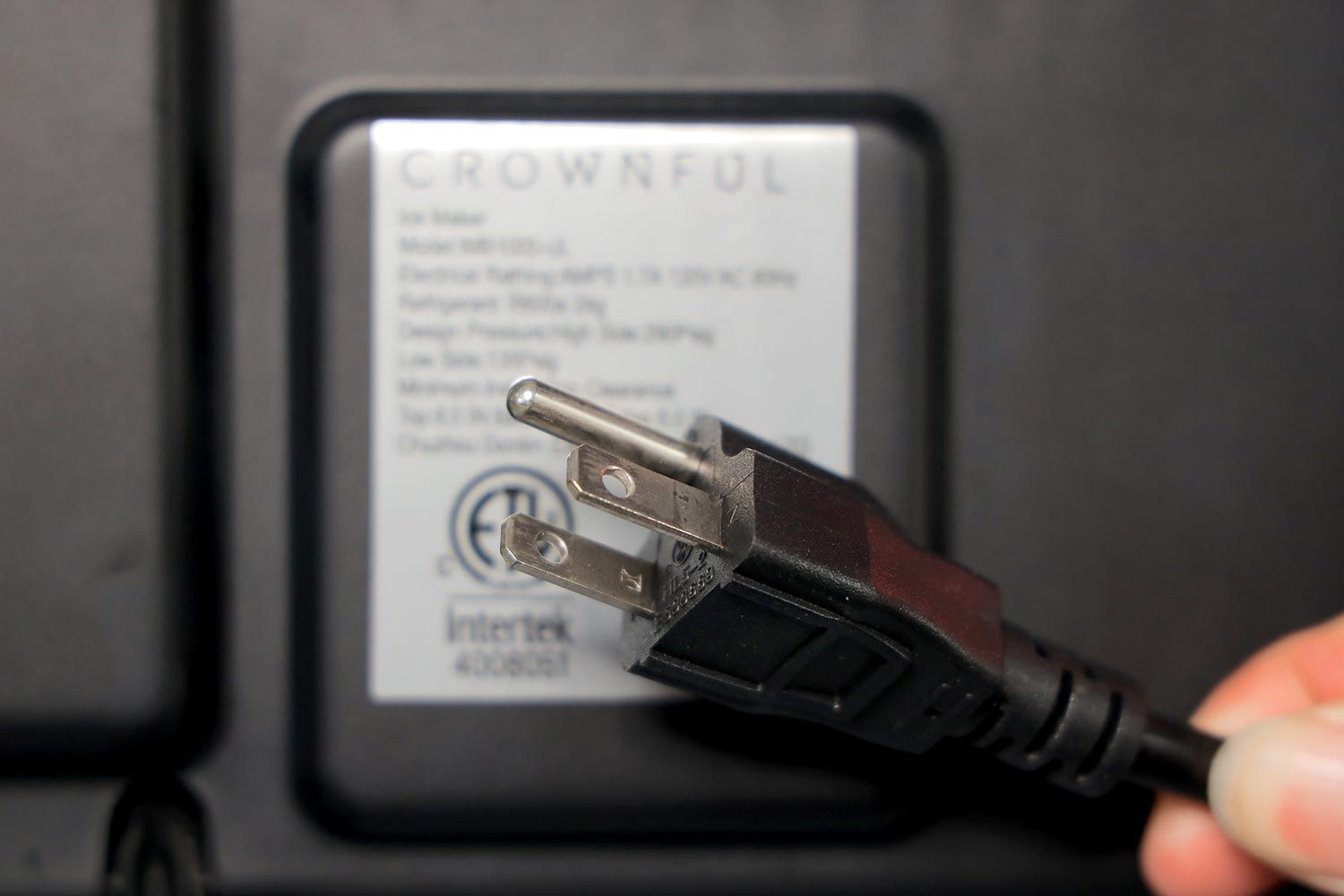 A three pronged plug being held up to the front of a portable ice maker.