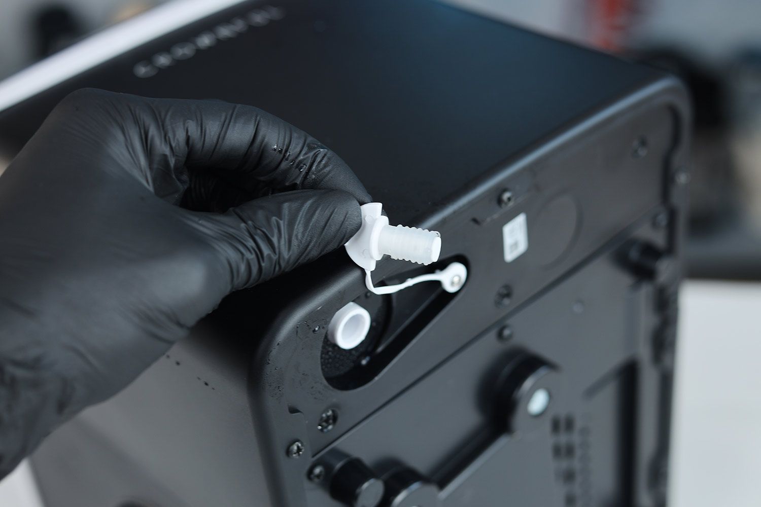 A hand holding the plug to a water reservoir on a countertop bullet ice maker.