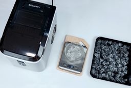 The EUhomy ice maker on the left, a bowl of broken on a scale measuring 30 grams, and a baking tray of well-formed ice to the right.