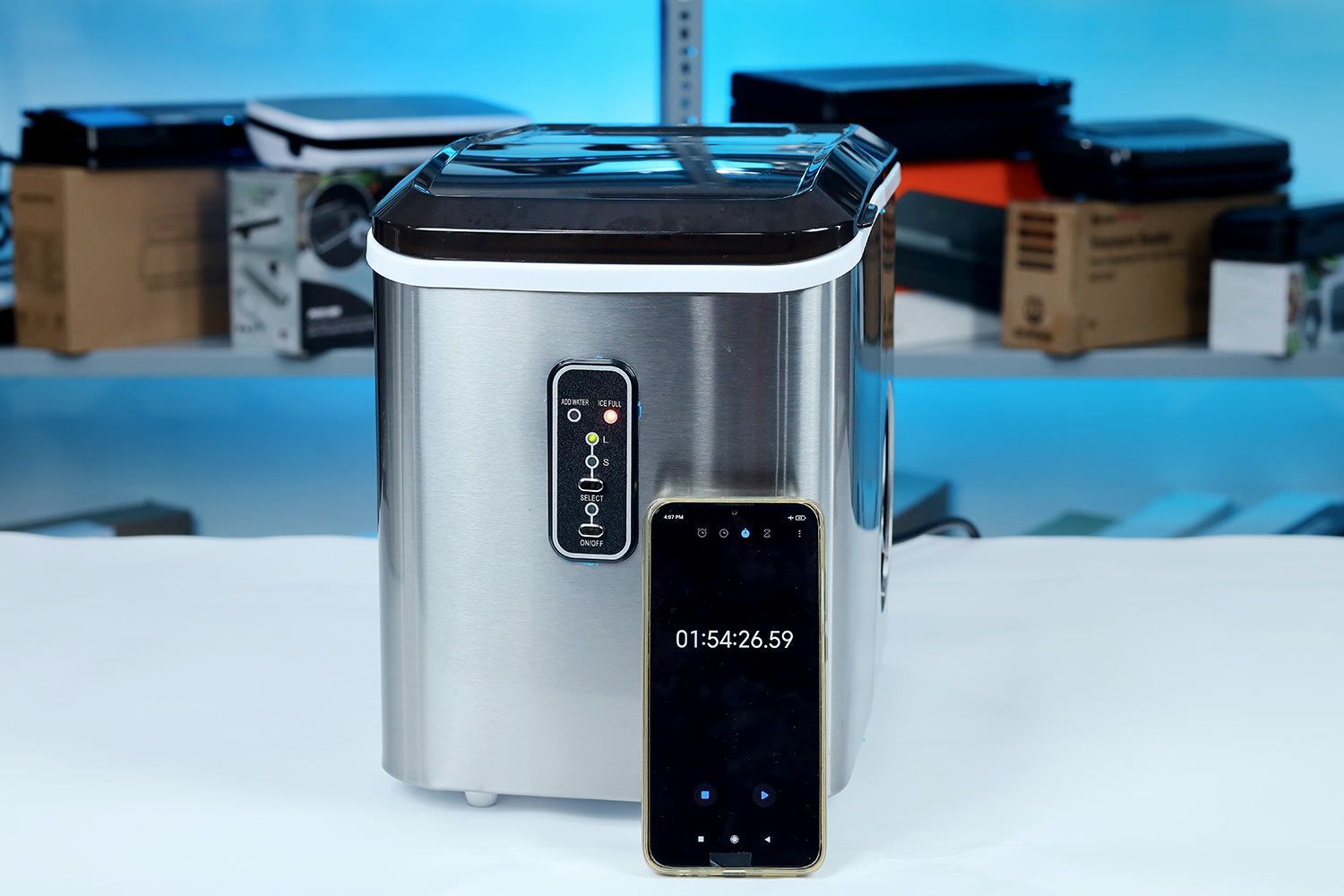 A stopwatch resting against the front body of the EUhomy countertop ice making and showing a time of 1 min 54 sec to fill a basket of ice.