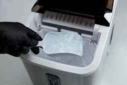 Bullet-shaped ice being scooped out of the basket of a countertop ice maker.