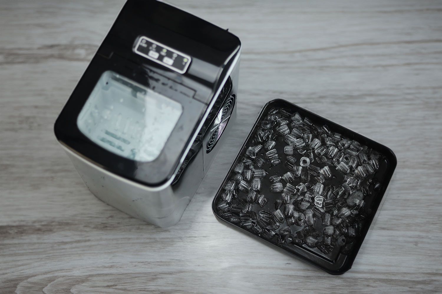 Ice in a baking tray next to a portable ice maker showing the quality of ice after leaving the machine running overnight.