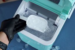 Ice being scooped up from an ice basket of a portable bullet ice maker.