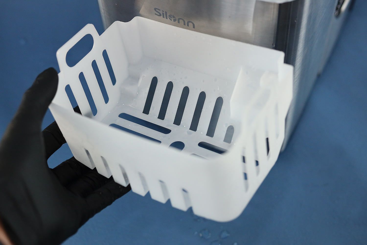 A hand holding up a plastic ice basket for a portable countertop ice maker.