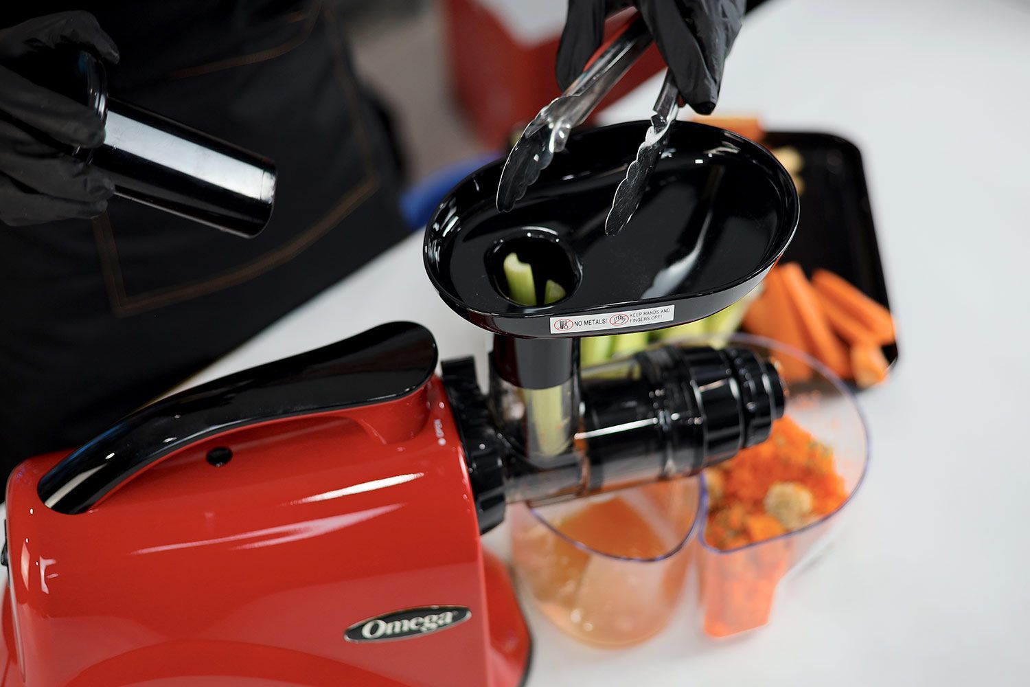 Person using a pair of tongs to feed masticating juicer