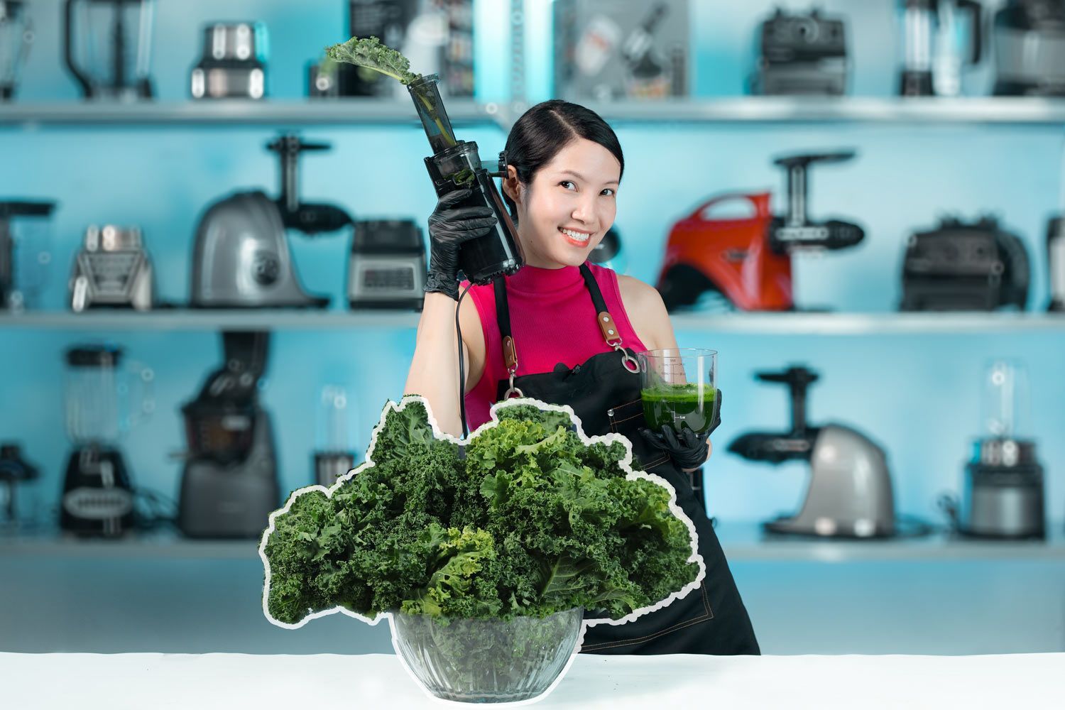 Smiling woman holding juicer in one hand, juice cup in the other, bowl of kale in the front