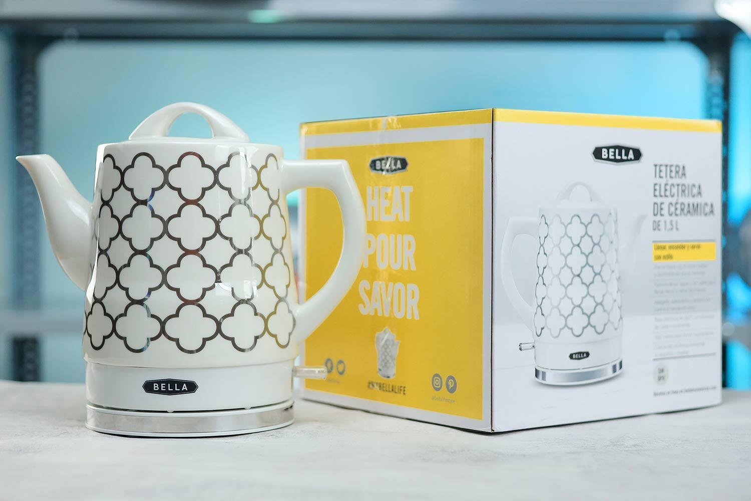 The Bella Ceramic Kettle 14745 on the left and its cardboard box on the right. In the background is a shelf with different electric kettles.