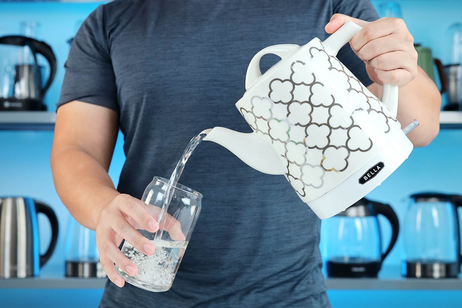 A person in a dark green shirt pouring water from the Bella Ceramic Gooseneck Electric Kettle (14745) into a glass.