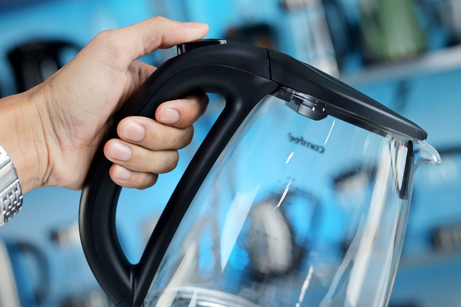 A hand holding the Comfee Glass Electric Kettle (CEKG003) by its handle.