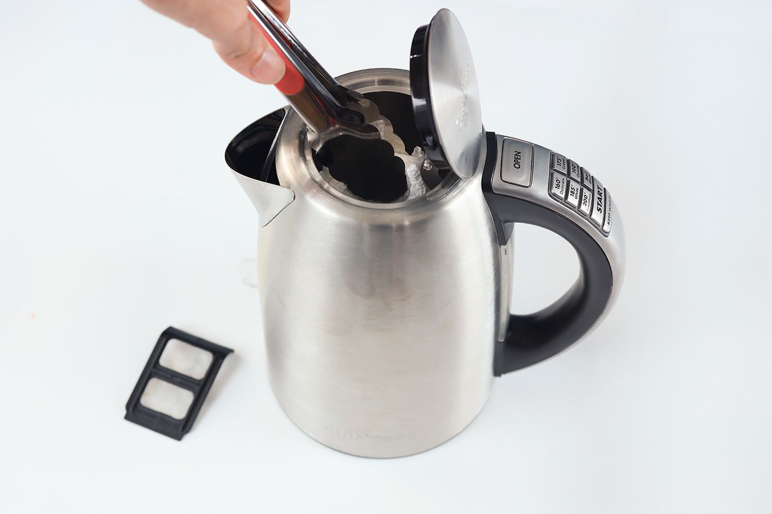 A hand using a kitchen tong to wipe the interior of the Cuisinart Stainless Steel Electric Kettle with 6 Preset Temperatures (CPK-17P1 PerfecTemp) with a tissue.