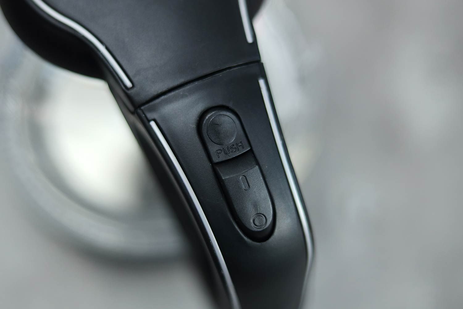 The handle of the Ovente Electric Glass Kettle (KG83B) has two buttons, the one above is the lid button and below is the power switch.