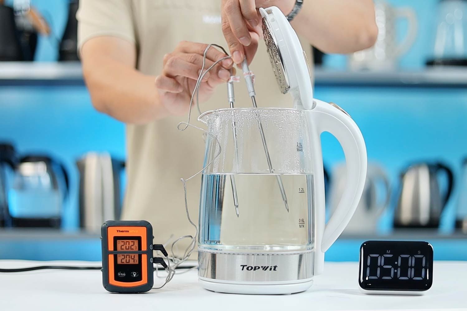 On the right is a Thermo Pro two-probe digital thermometer displaying 202°F and 204°F. In the middle is the Topwit Glass Electric Tea Kettle T630 with 1.5 liters of water and two probes inside. On the right is a digital timer on a 5 minute countdown.