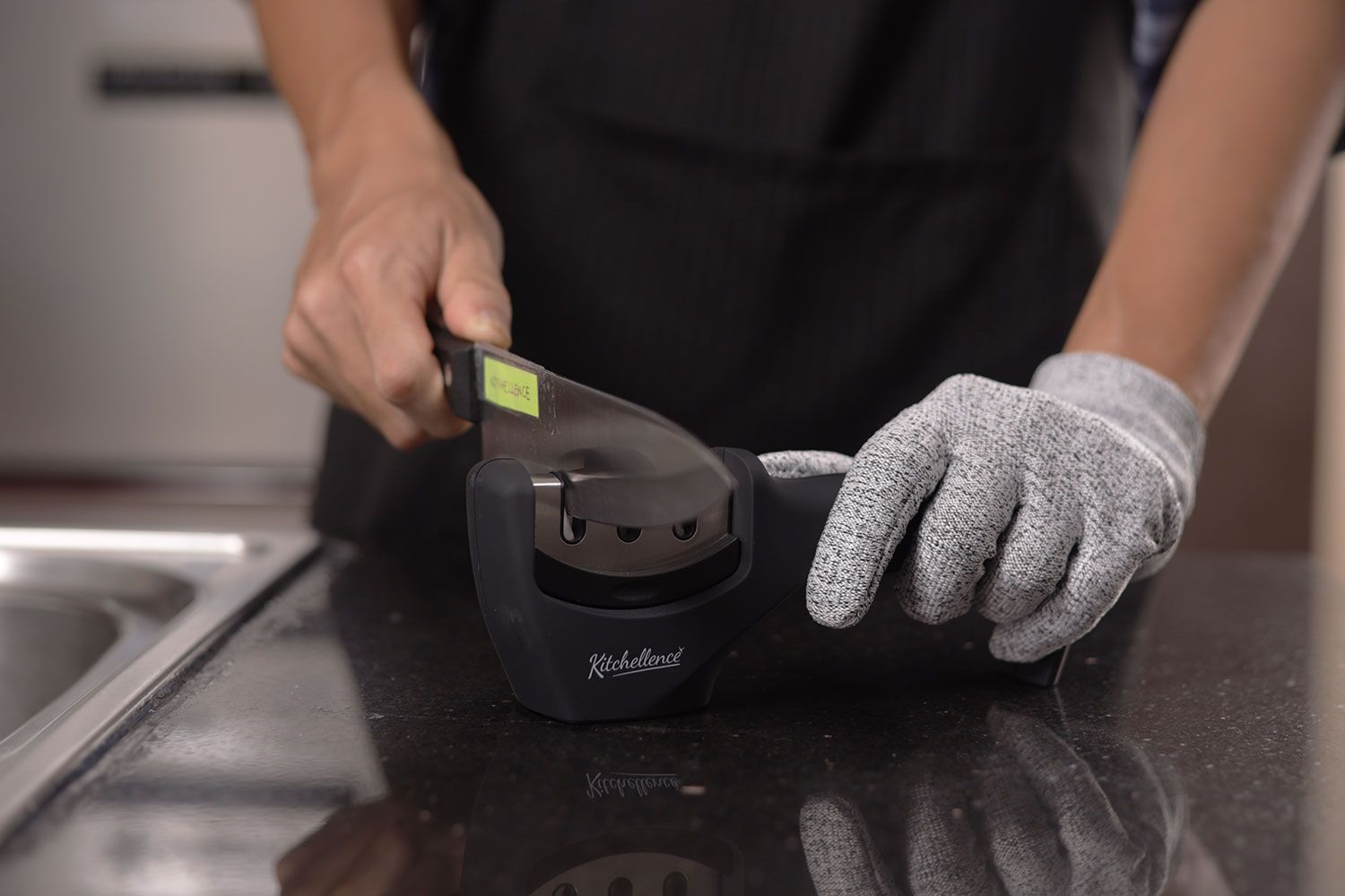 a person wearing a glove in one hand sharpening a kitchen knife with the Kitchellence on a countertopa person wearing a glove in one hand sharpening a kitchen knife with the Kitchellence on a countertop