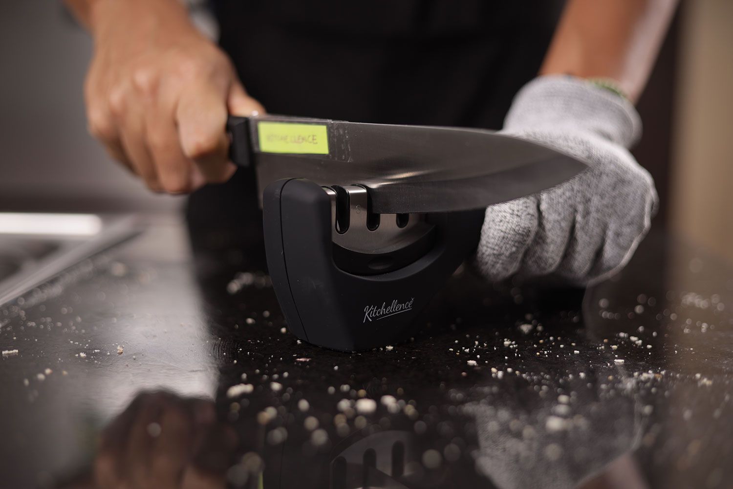 a person wearing a glove in one hand sharpening a kitchen knife with the Kitchellence on a salt-sprinkled countertop