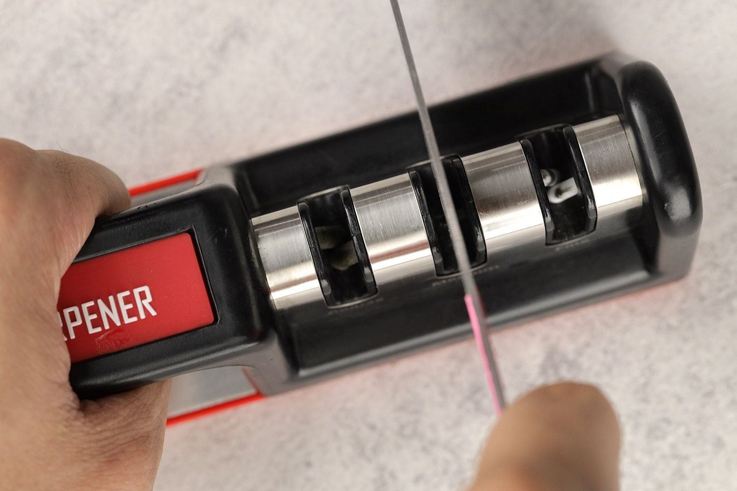 Top view of a knife being sharpened with the Cubikook, the sharpener being held in one hand